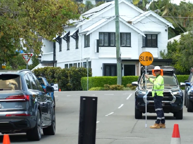 Traffic control worker using slow bat to manage vehicle flow during roadwork operations on a residential street