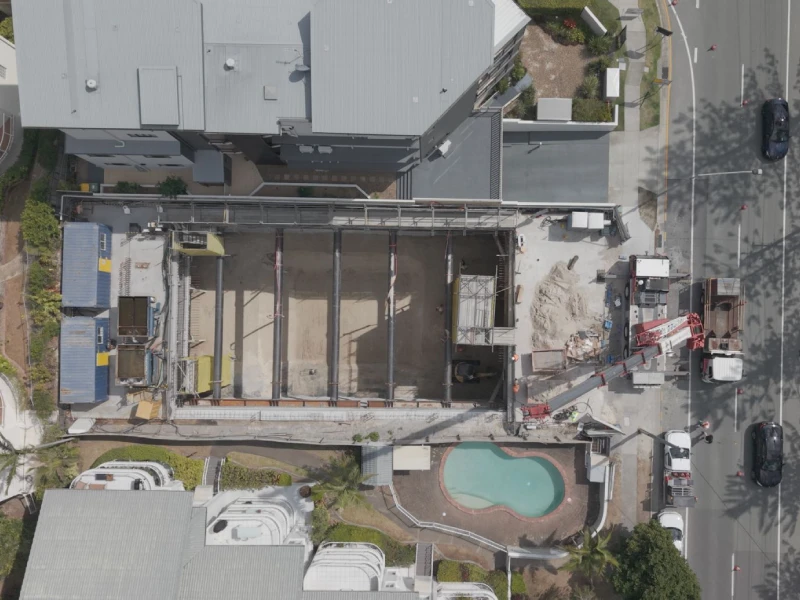 Aerial view of an active construction site with building works, excavation equipment, and surrounding urban development